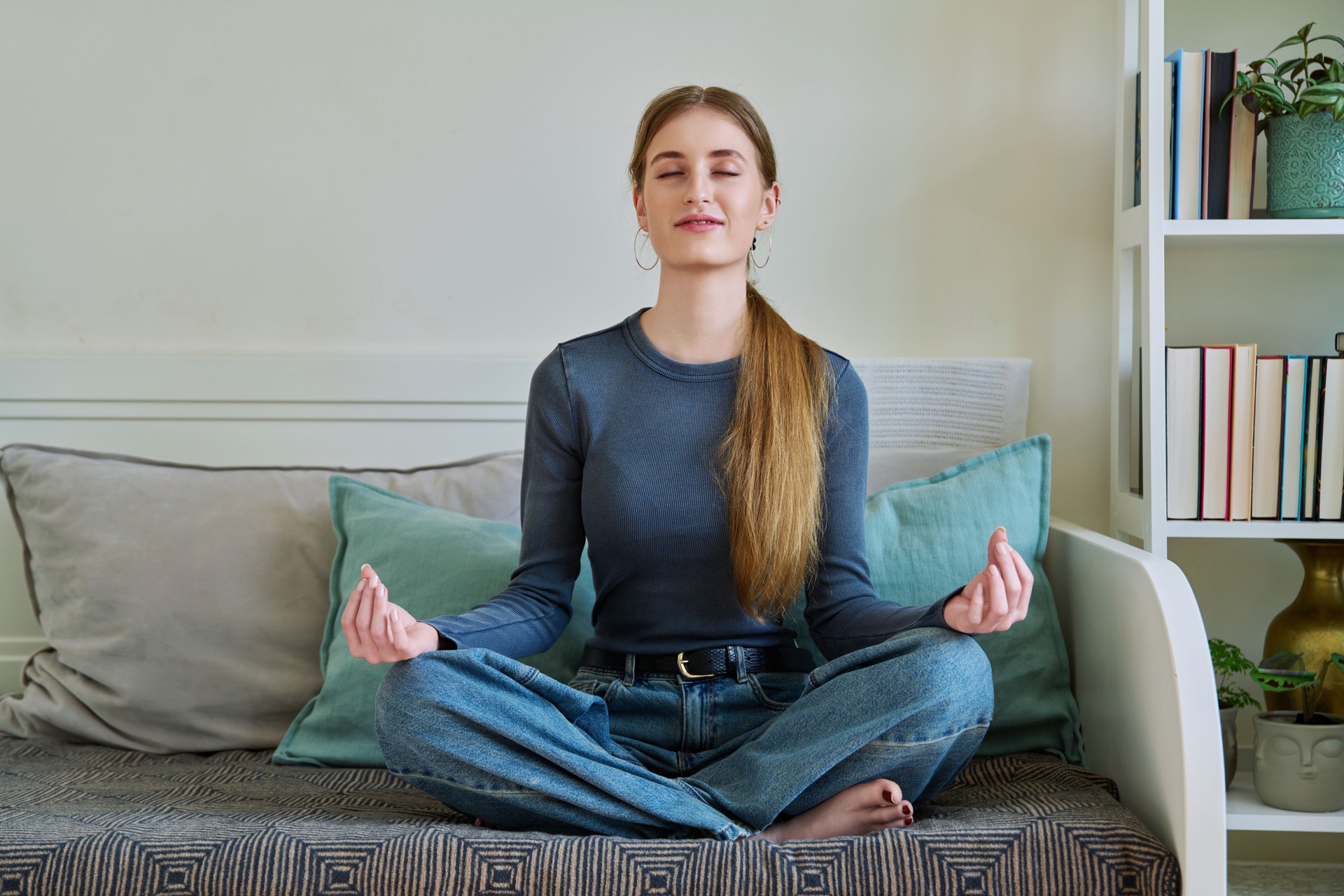 Young teenage relaxed female sitting in lotus position, meditating at home