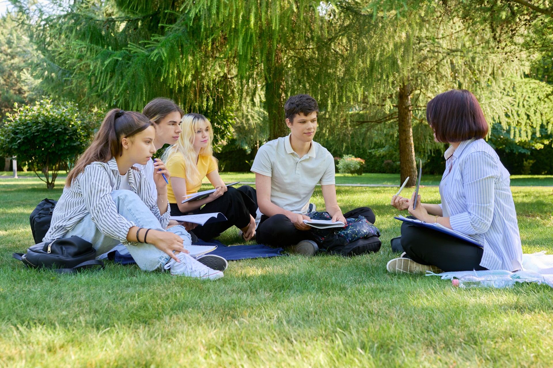 Outdoor, group of students with female teacher sitting on grass